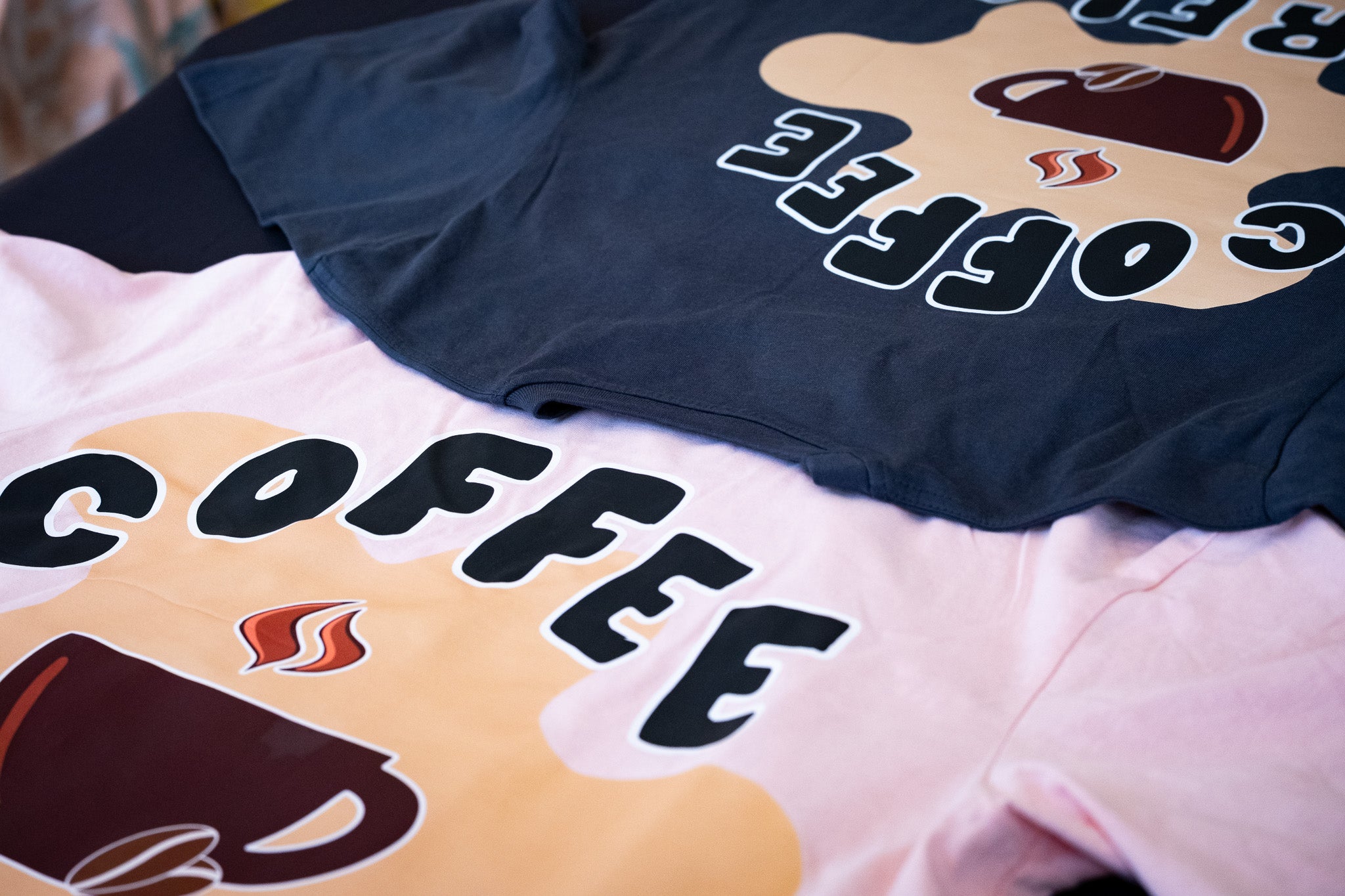 Two t-shirts with coffee-themed designs on a surface