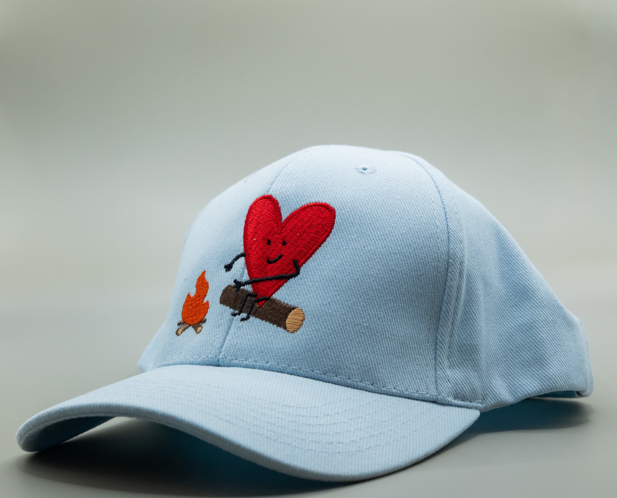 Light blue cap with a red heart and small dog design on a neutral background