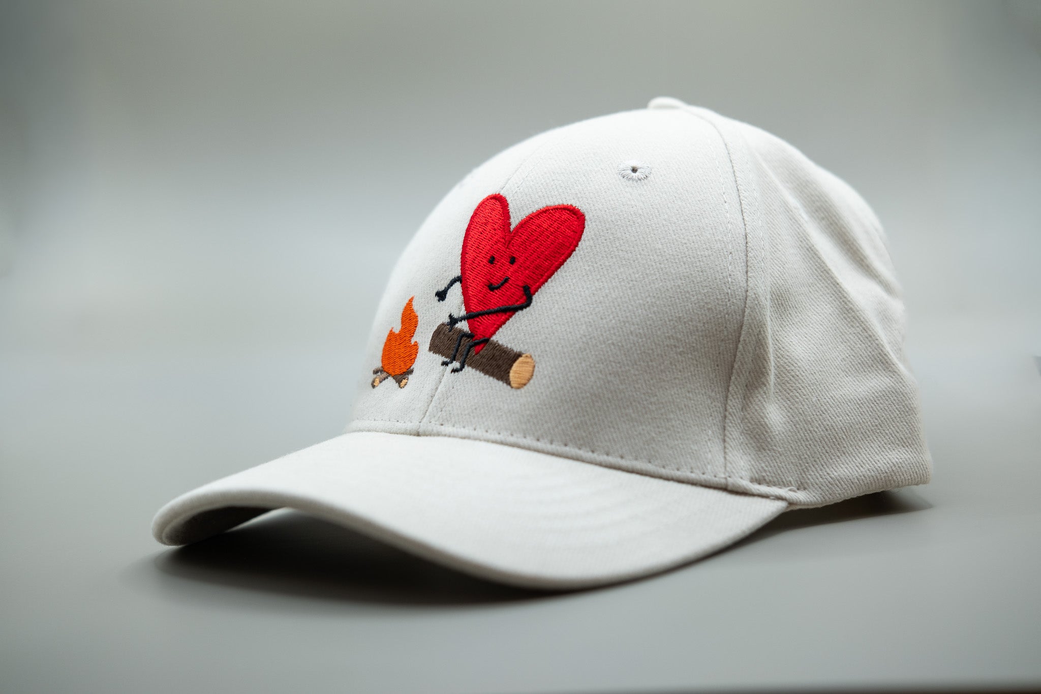 White cap with a red heart and cartoon design on a gray background