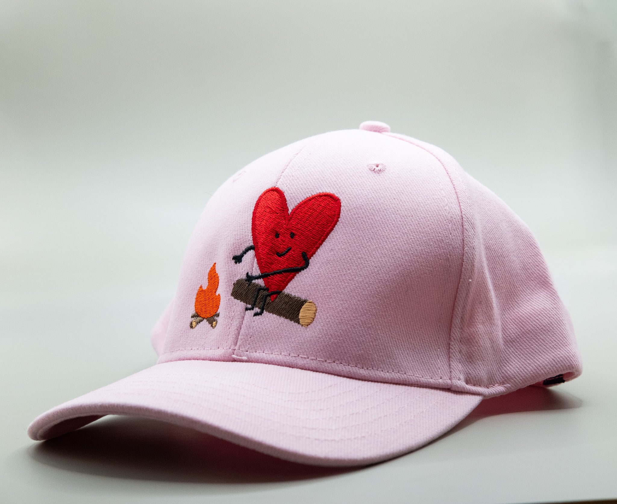 Pink cap with a heart design and small figures on a light gray background