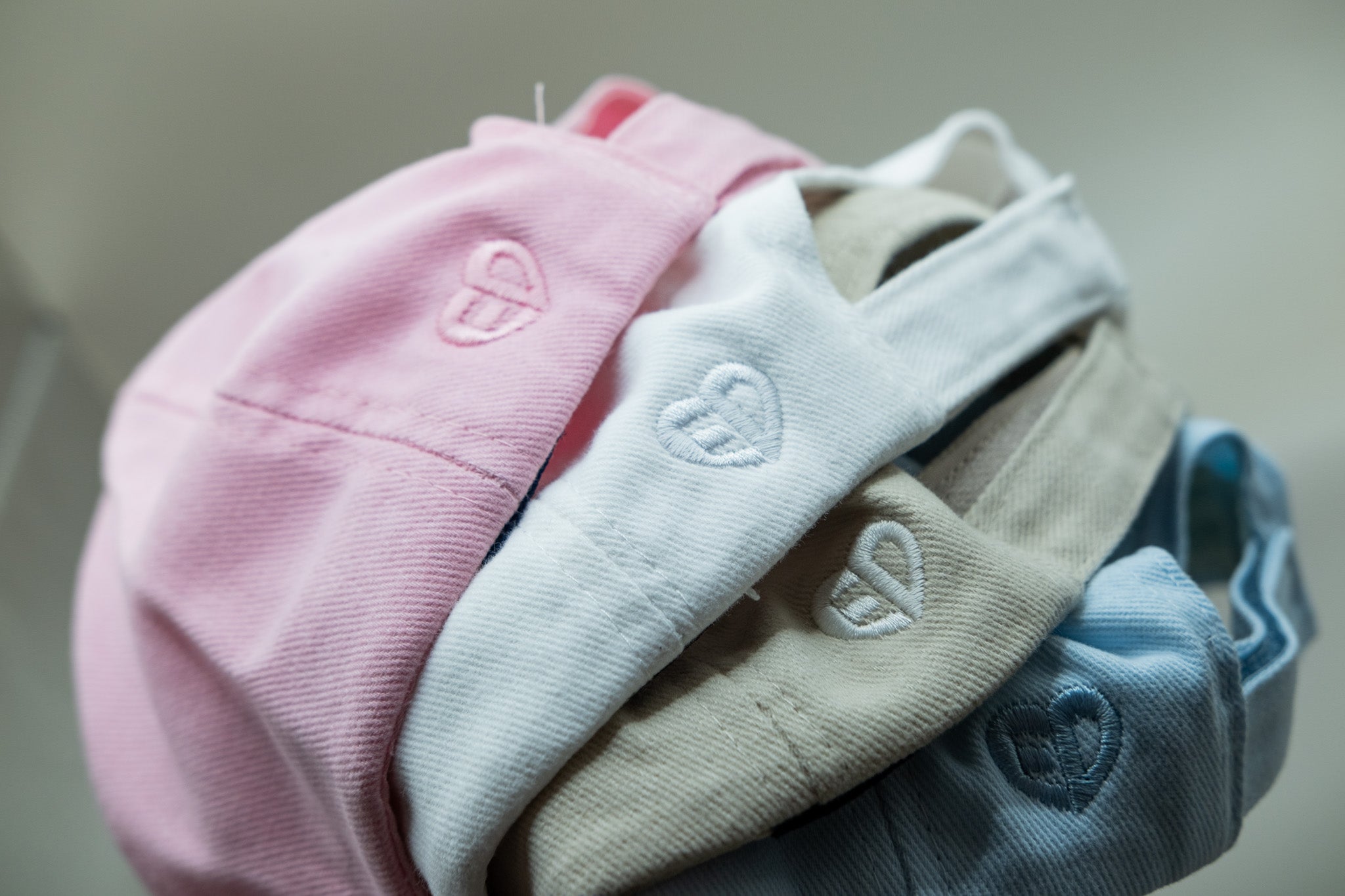 Stack of baby hats in pink, white, beige, and blue with heart designs on a neutral background.