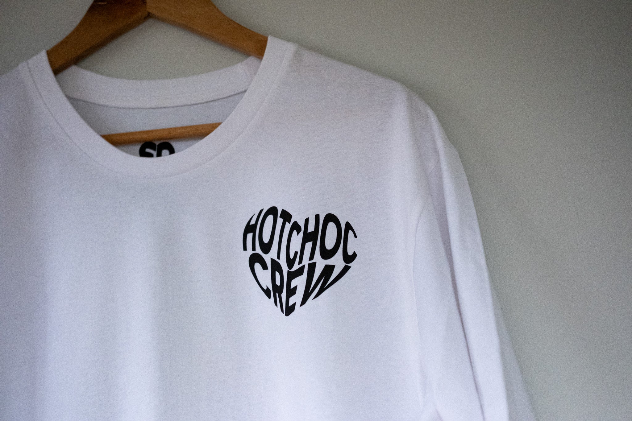 White sweatshirt with 'Hotchoc Crew' text on a hanger against a plain background